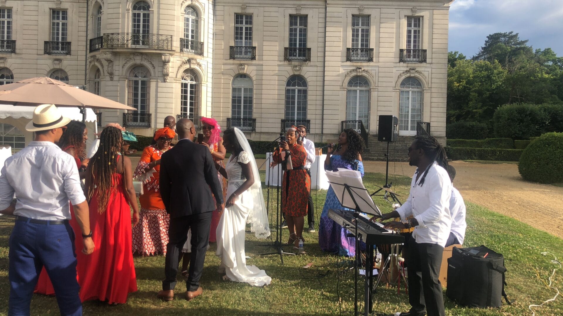 Invités réunis sous une pergola pour un cocktail de mariage élégant en extérieur, entourés de verdure et d’une bâtisse en pierre.