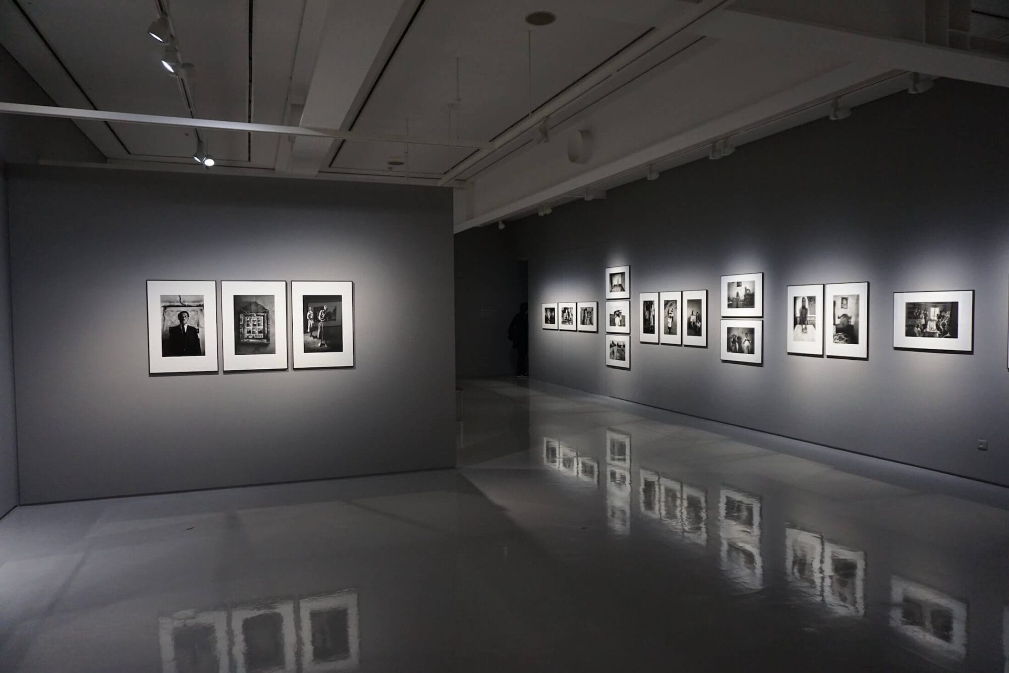 Galerie d'art moderne avec des photographies en noir et blanc encadrées, exposées sur des murs gris avec un éclairage soigné.