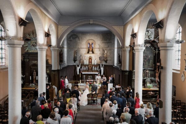 Vue d’ensemble d’une cérémonie de mariage dans une église, avec les mariés debout devant l’autel, entourés de l’assemblée et des officiants religieux.