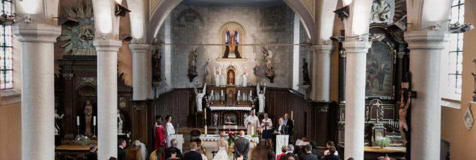 Vue d’ensemble d’une cérémonie de mariage dans une église, avec les mariés debout devant l’autel, entourés de l’assemblée et des officiants religieux.