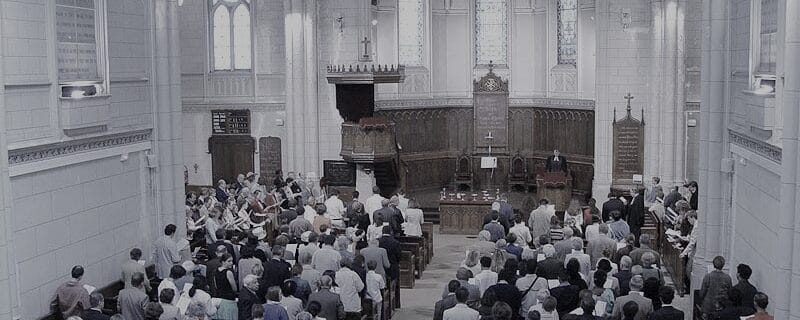 Une assemblée de fidèles debout dans une grande église gothique pendant un office religieux.