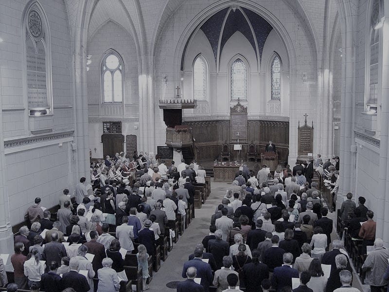 Une assemblée de fidèles debout dans une grande église gothique pendant un office religieux.