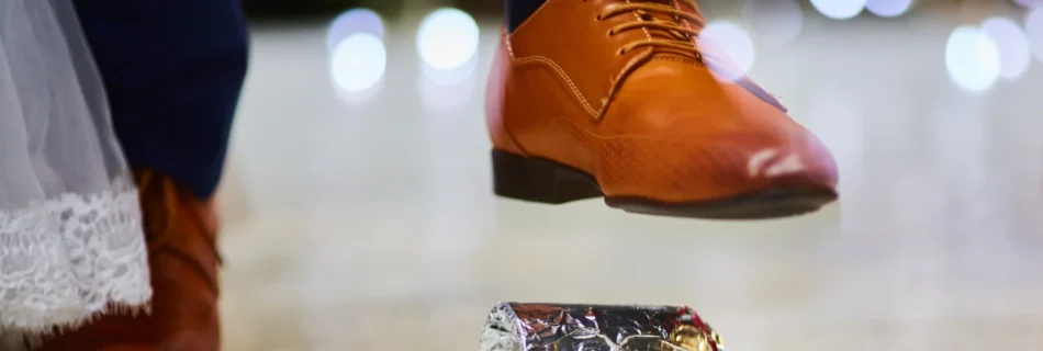 Un homme en costume bleu et chaussures marron écrasant un objet enroulé dans du papier aluminium lors d'une cérémonie de mariage.