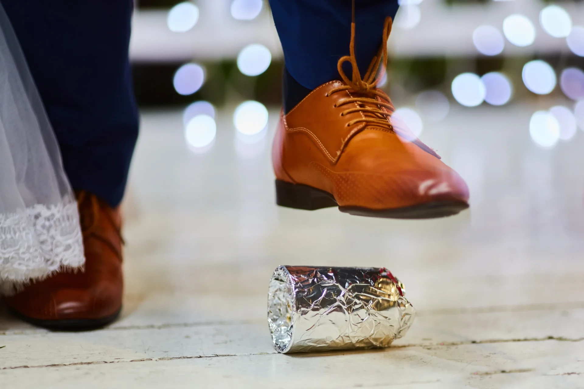 Un homme en costume bleu et chaussures marron écrasant un objet enroulé dans du papier aluminium lors d'une cérémonie de mariage.