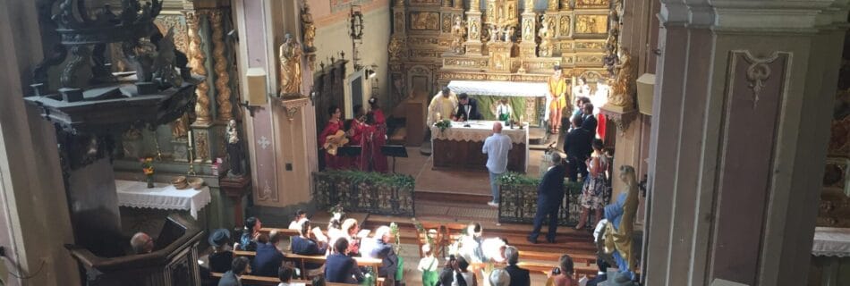 Vue d’ensemble d’une église richement décorée où se déroule une cérémonie de mariage, avec une chorale gospel en robes rouges chantant près de l’autel et une assemblée réunie dans les bancs.