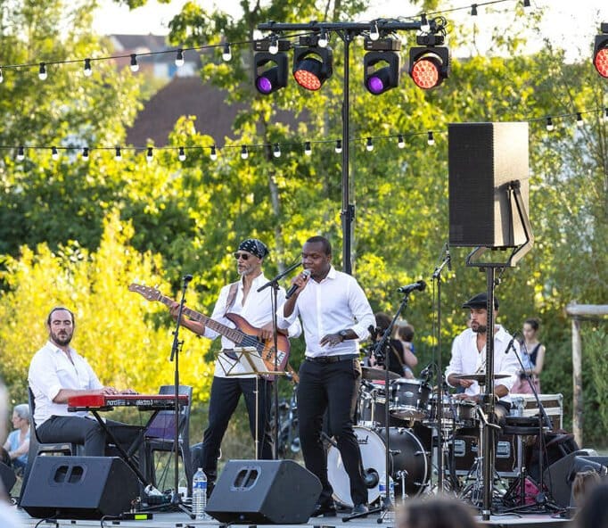 Groupe de musiciens jouant en live lors d’un concert en plein air avec éclairages et ambiance festive.