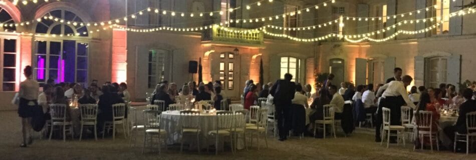 Réception nocturne en extérieur avec tables élégamment dressées, guirlandes lumineuses suspendues et un château illuminé en arrière-plan.