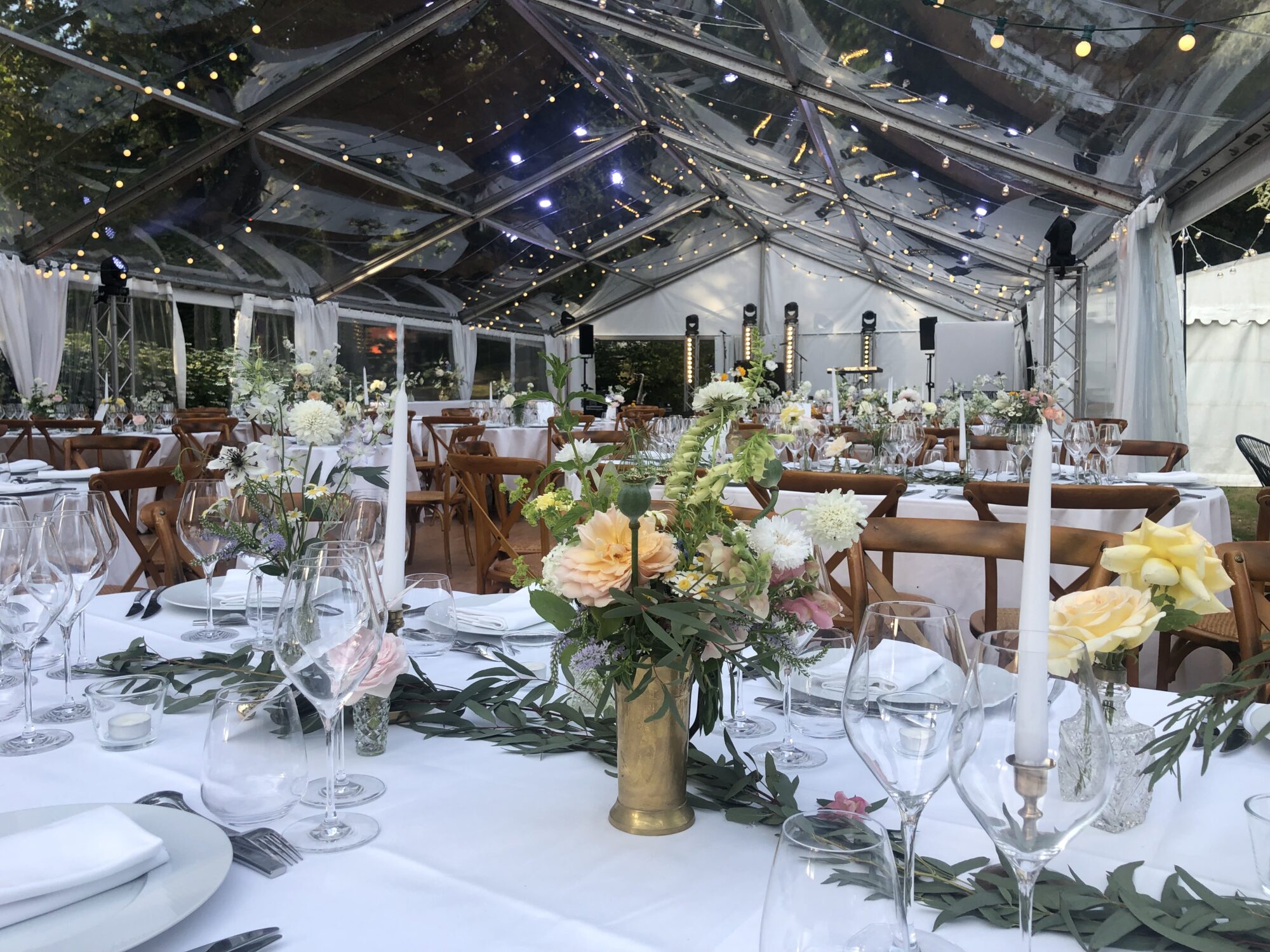 Table élégamment dressée sous une tente transparente illuminée, avec décor floral raffiné et chandelles pour une réception de mariage.