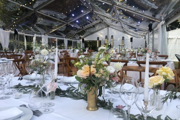 Table élégamment dressée sous une tente transparente illuminée, avec décor floral raffiné et chandelles pour une réception de mariage.