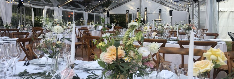 Table élégamment dressée sous une tente transparente illuminée, avec décor floral raffiné et chandelles pour une réception de mariage.