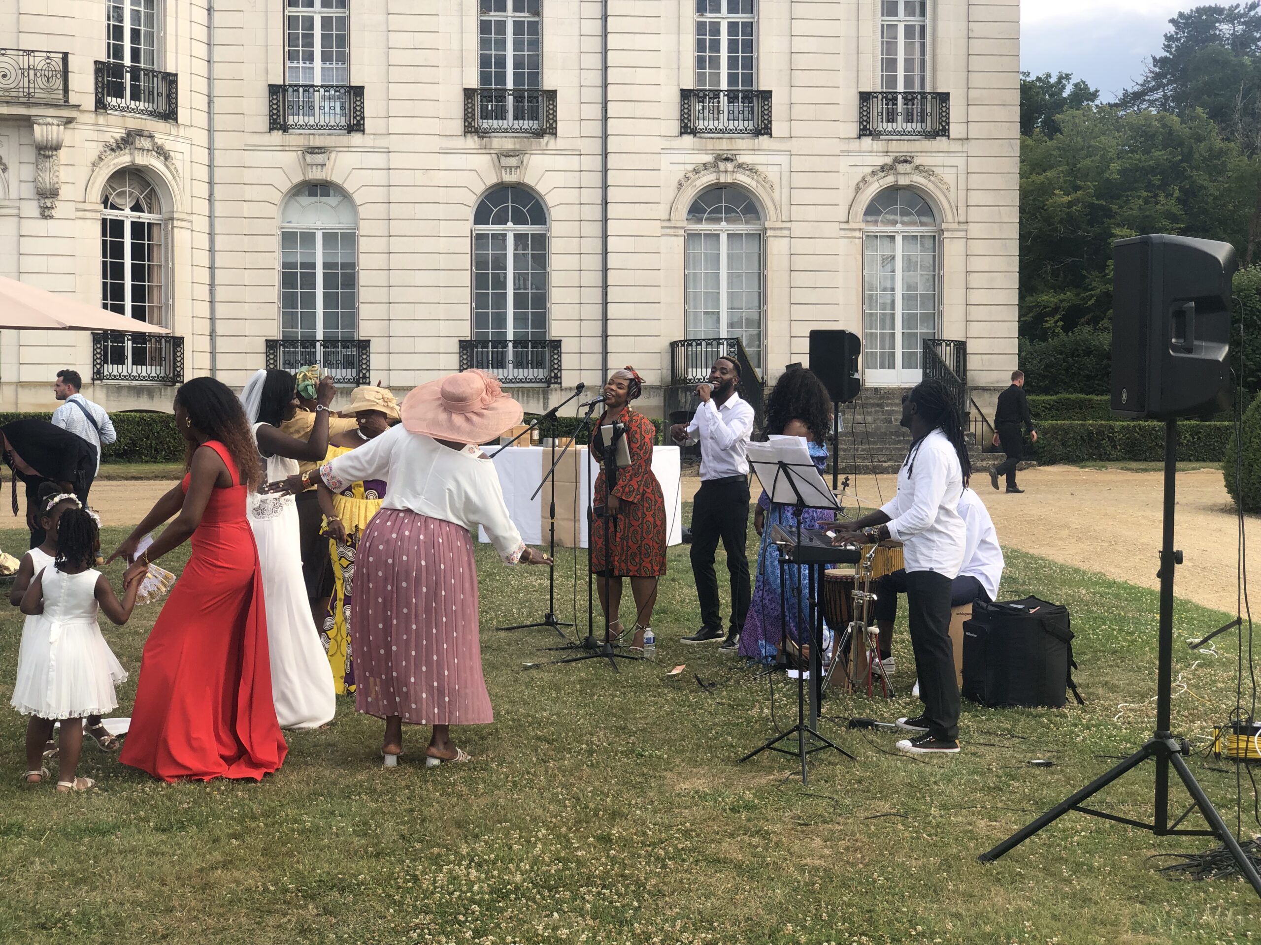 Mariage en plein air avec un groupe de musiciens et chanteurs animant la réception. La mariée en robe blanche danse entourée de ses proches vêtus de tenues colorées, tandis que les artistes chantent et jouent des instruments.