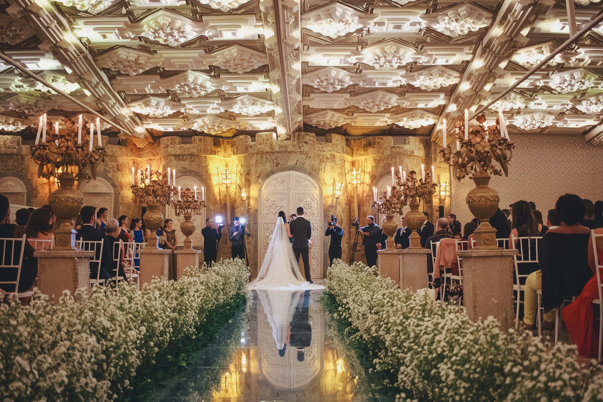 Mariage somptueux dans une salle luxueuse, avec les mariés au centre d’un décor fleuri et élégant entourés d’invités.